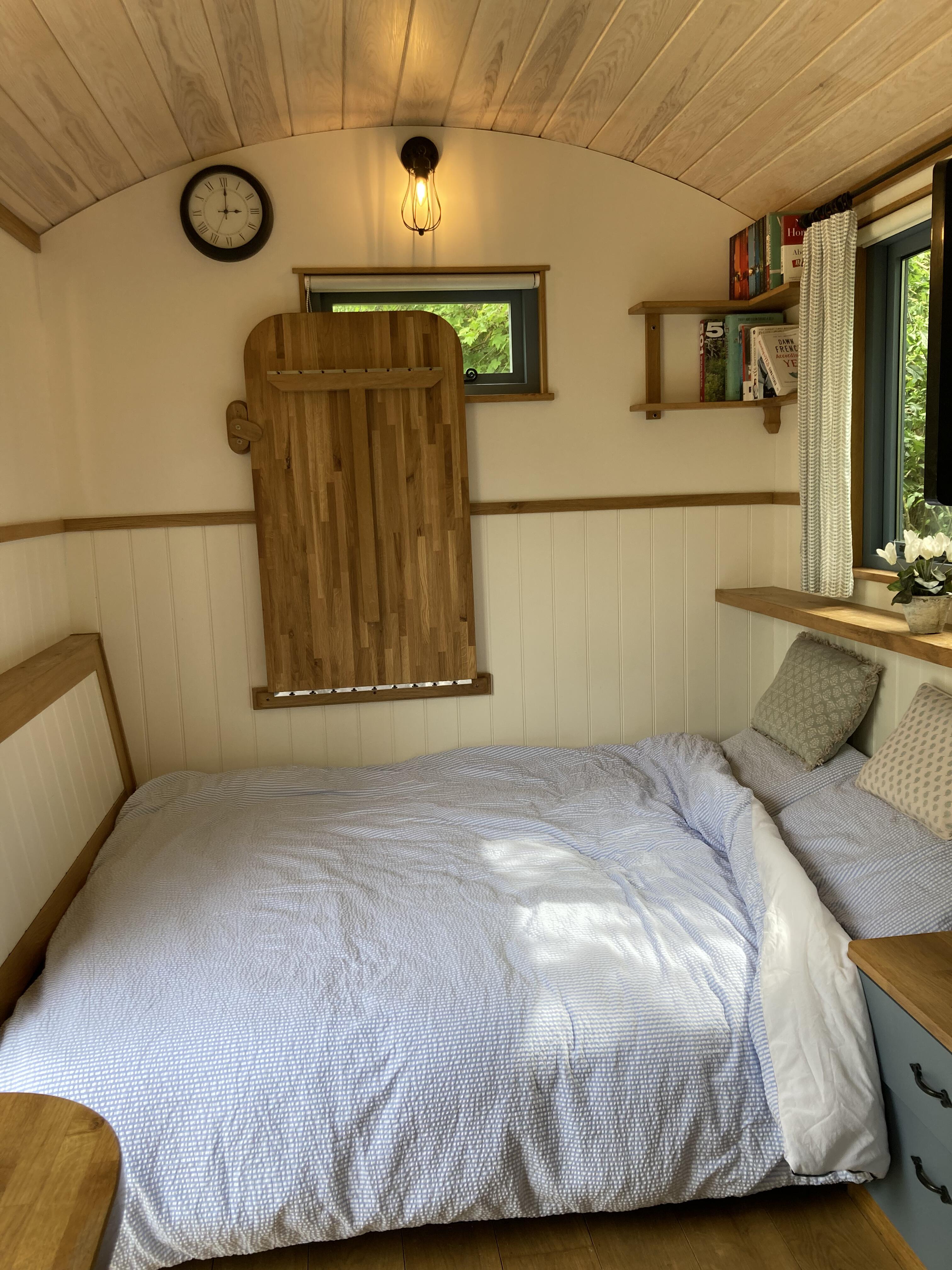 The double bed made up with white bedding, cushions and a bookshelf beside the window.