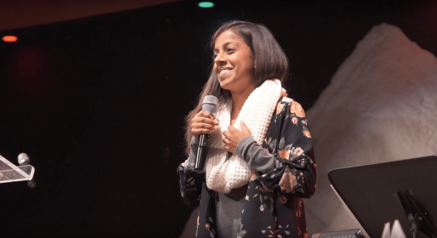 Joyce stands with a microphone in one hand and her other hand pressed against her heart. Her gaze radiates love as she looks out at the crowd—a love that reflects the compassion and grace of Jesus.