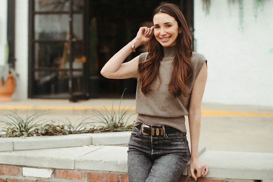 Blaine in a tan top, seated on a brick wall, smiling