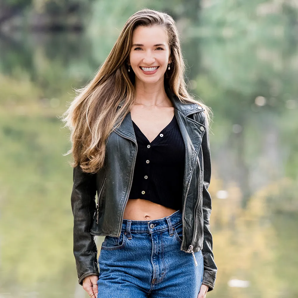 Photo of Sydney in a black top and leather jacket, hands at her sides, smiling