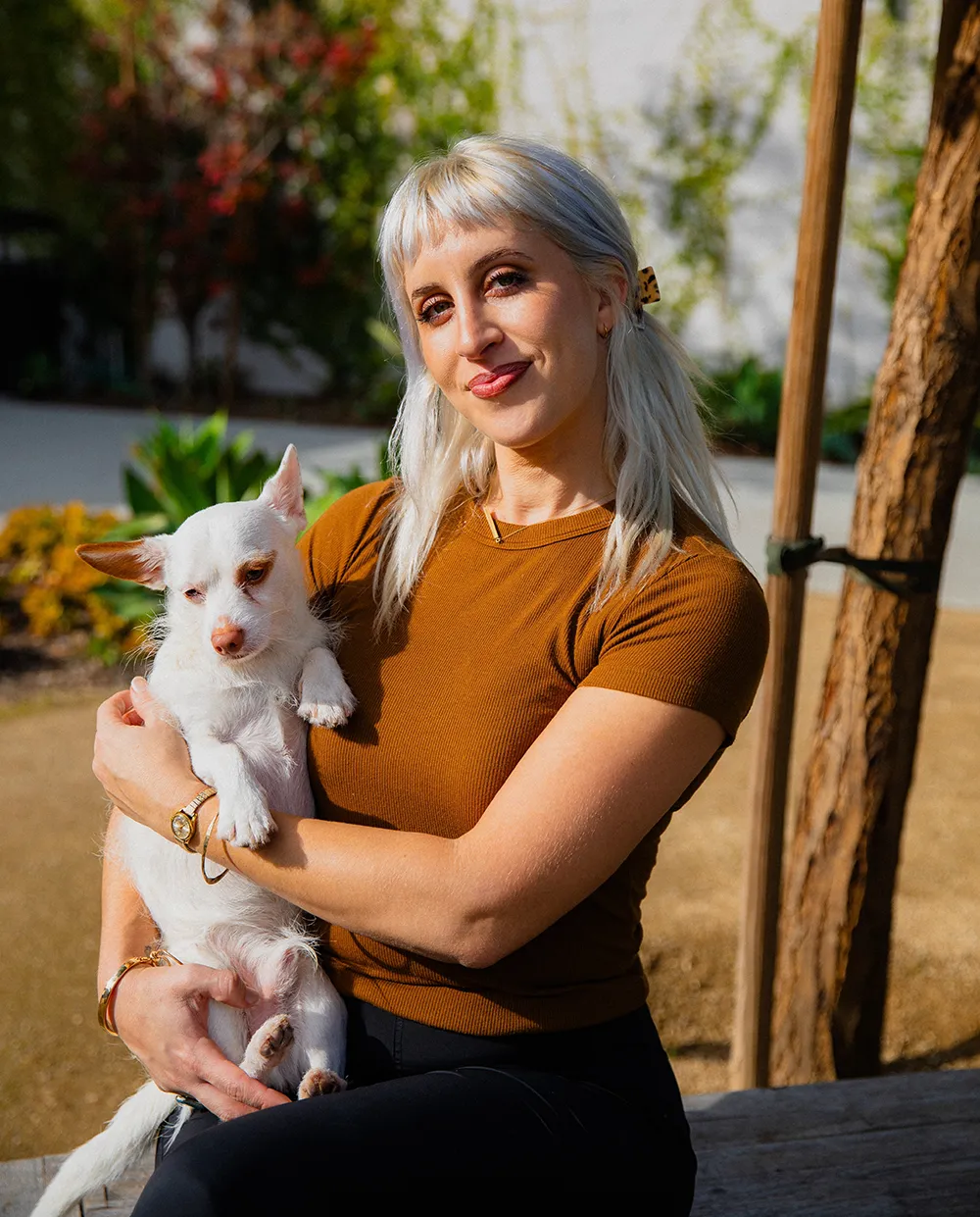 Photo of Merav in a dark orange shirt, holding her dog, smiling