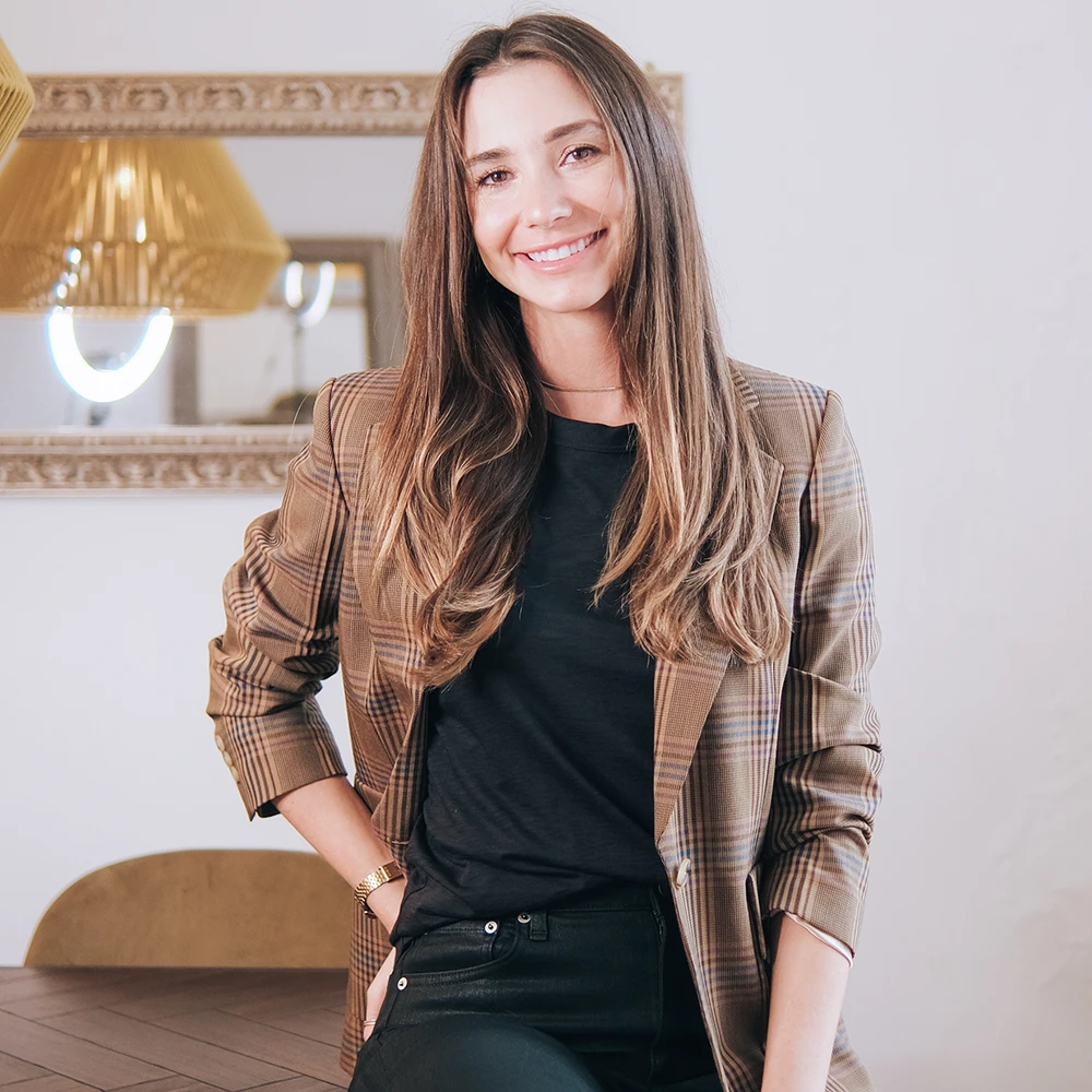 Blaine wearing a tan blazer, and black top, seated, smiling