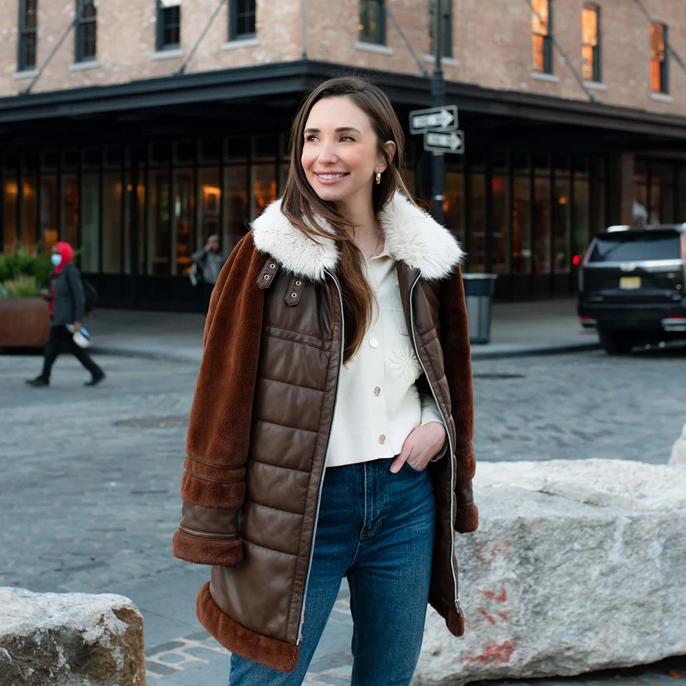 Blaine, wearing a white button-up shirt and beige skirt, standing indoors, smiling.