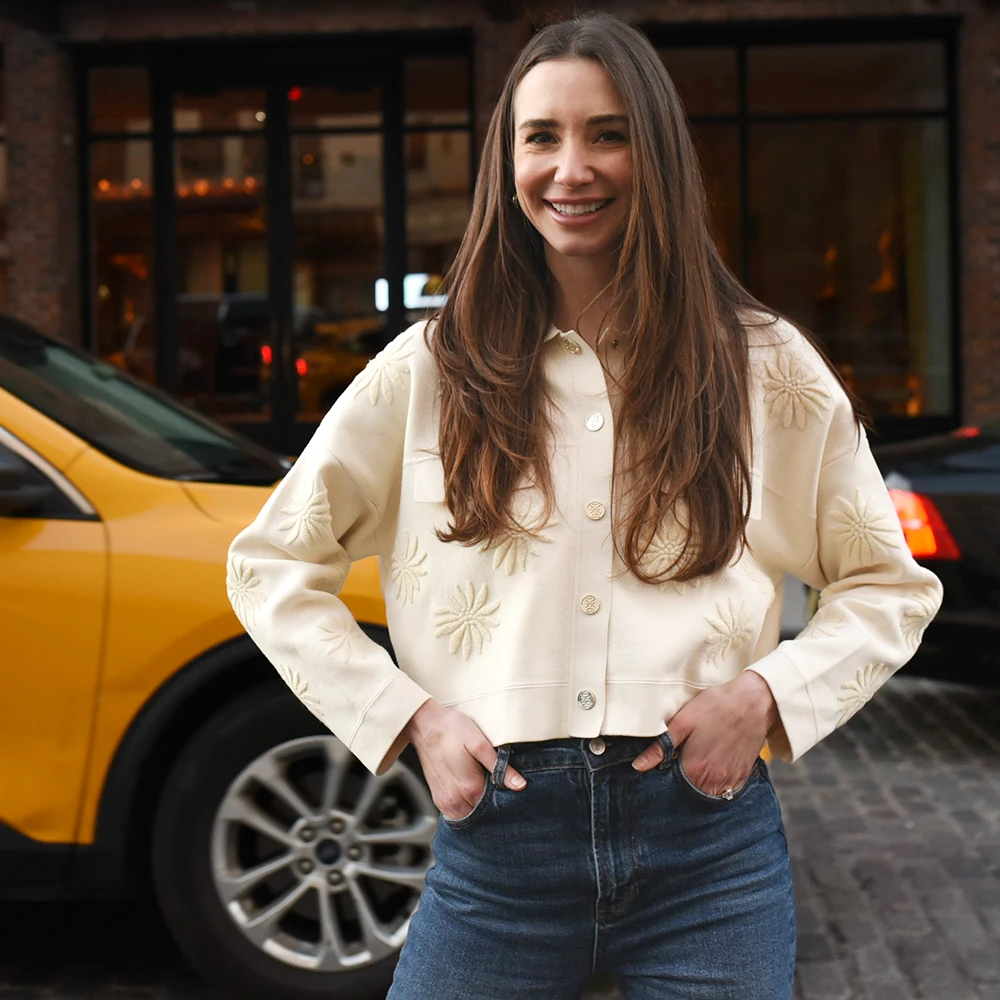 Blaine, wearing a white button-up shirt and beige skirt, standing indoors, smiling.