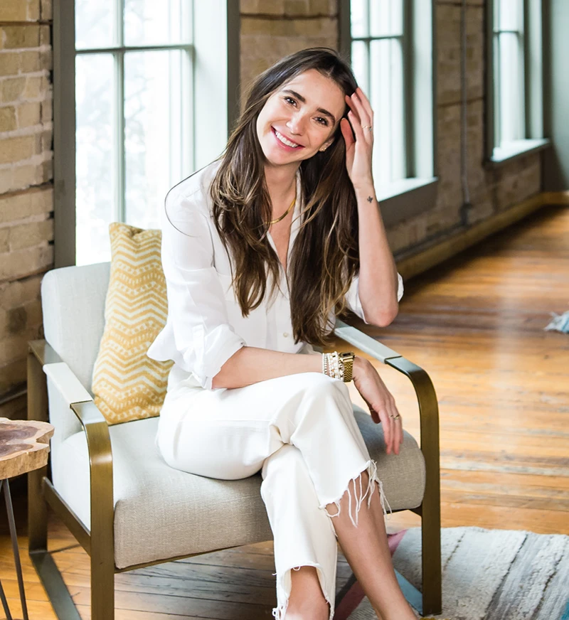 Blaine, wearing a white button-up shirt and beige skirt, standing indoors, smiling.