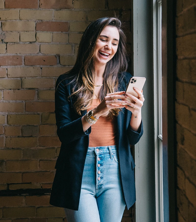 Photo of Blaine in a navy blazer and blue jeans, holding her phone, smiling
