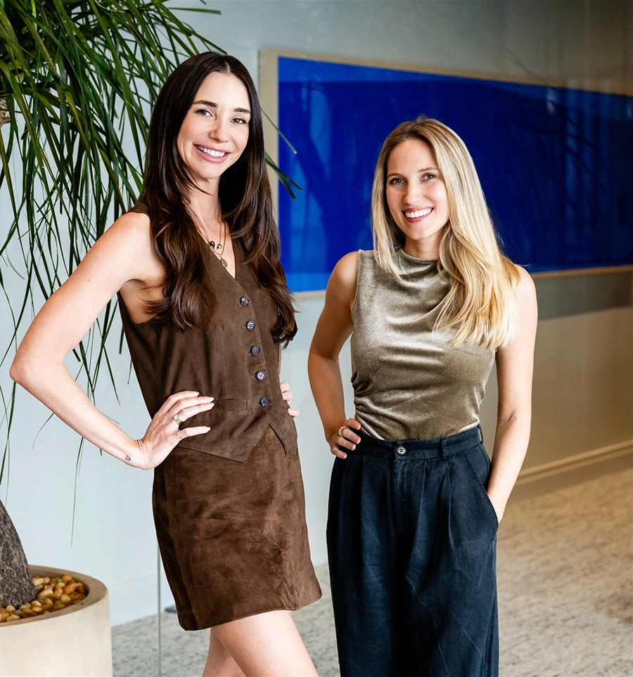 Photo of Brianna, in a gold top and navy pants, standing next to Blaine in a brown dress, both smiling
