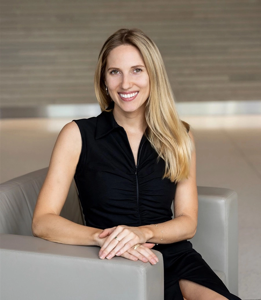 Photo of Brianna in a Black dress, seated in a grey chair, smiling