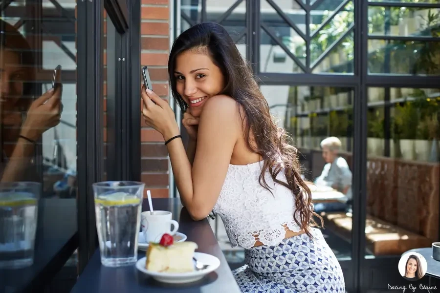 A woman with a white top, has a long hair and is smiling to someone, not looking at her phone