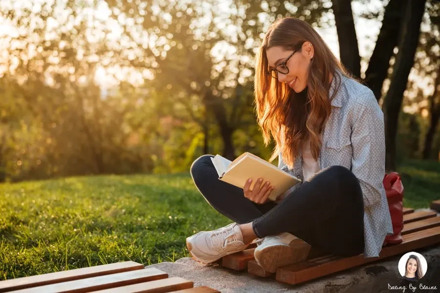 A woman wearing glasses is reading a book in the park