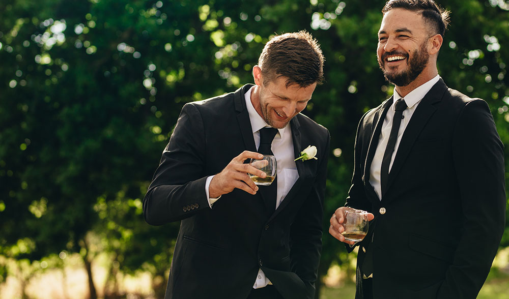 Two men smiling in tuxedos at a wedding