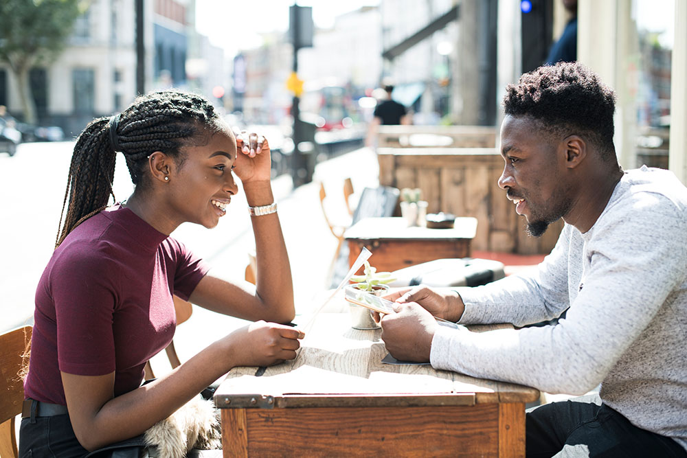 Man and woman sitting at table outside, smiling, on a date