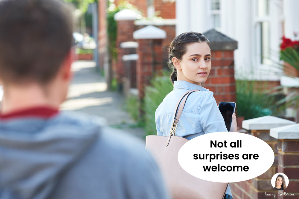 Photograph of a street in daylight, with man's back in foreground, with woman in background facing toward the lens, with a confused look on her face
