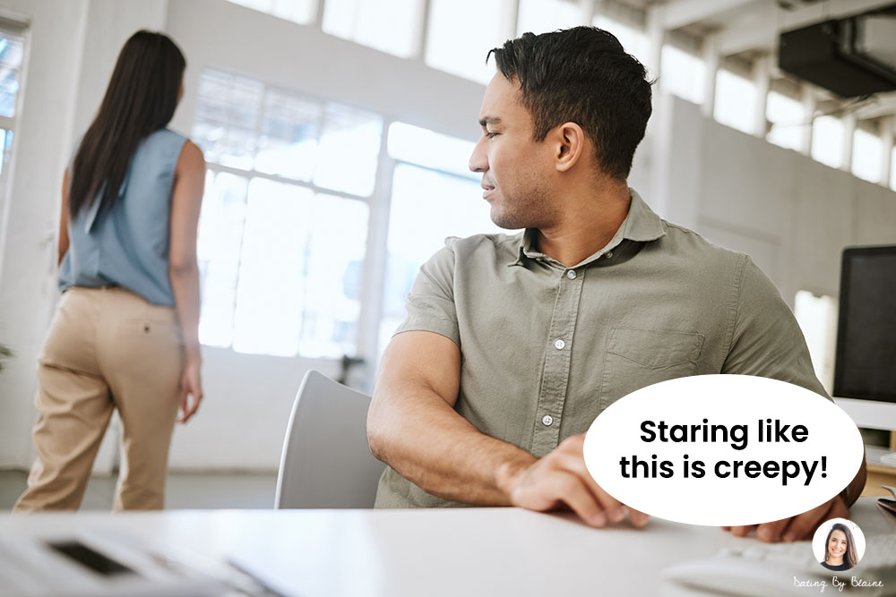 Man seated at desk, turning around to stare at a woman walking by's rear end