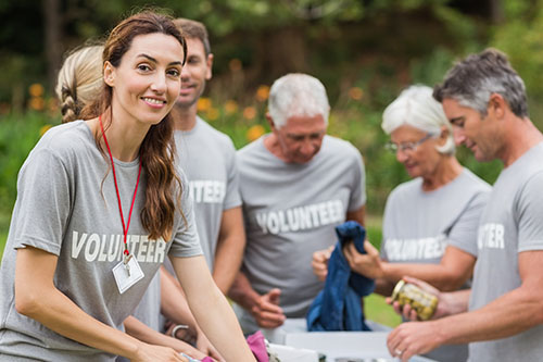 Brunette woman wearing a t-shirt with the word volunteer printed on it, placing canned goods into a bin