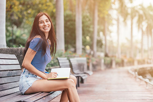 Brunette woman seated on bench on a university campus with a notebook on her lap