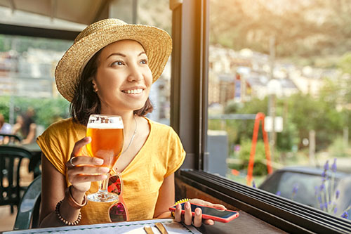 Stylish Asian woman seated in a restaurant holding a beer and smiling