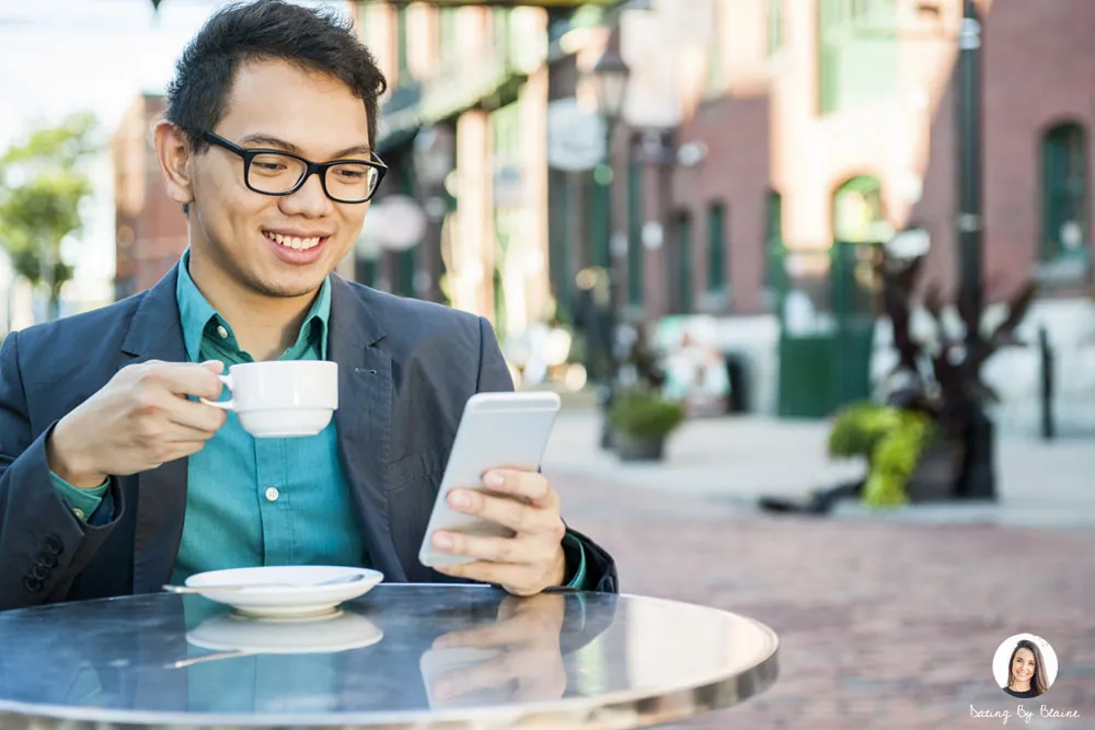 Man of Asian descent wearing a blazer at a cafe smiling at his phone