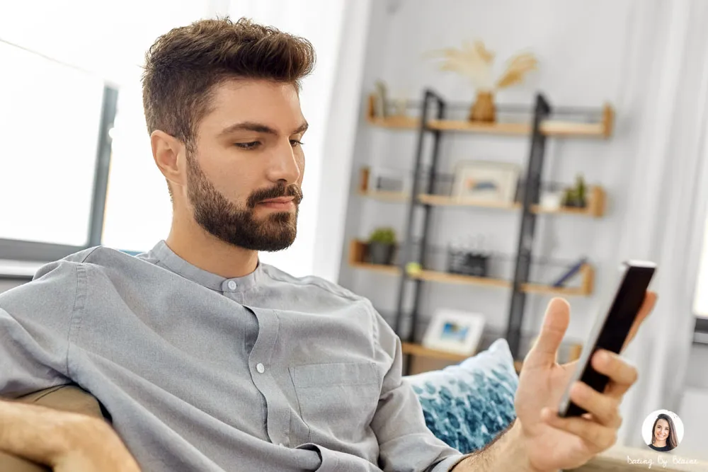 Man with short brown hair sitting on couch, looking at his phone