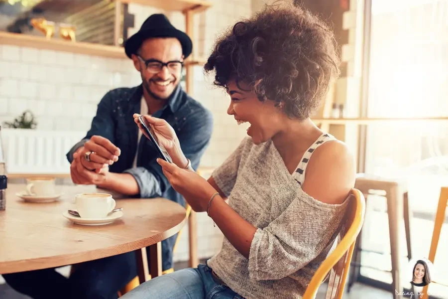 A man and a woman seated at a table in a well-lit cafe, laughing about a joke