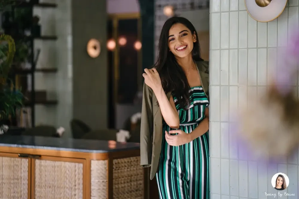 A pretty girl of Indian descent in what looks like an upscale restaurant, touching her hair, looking into the camera