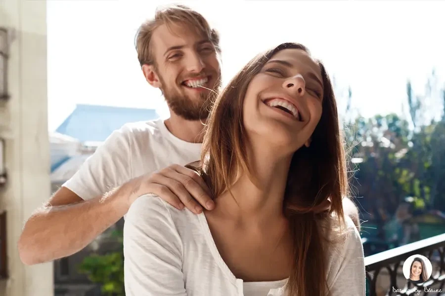 Man smiling, as he massages the shoulders of a woman in front of him, who is also smiling