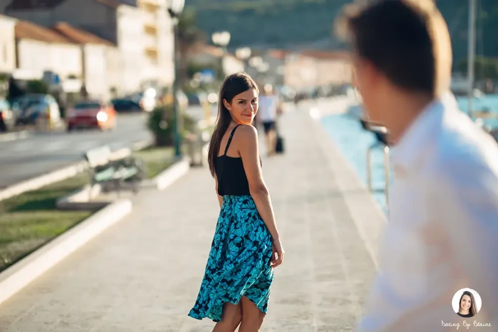 A girl wearing a dress looking at the boy wearing a white polo in a distance