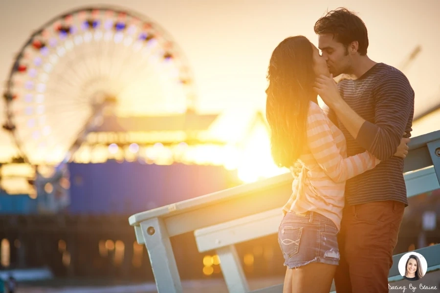 Man and woman standing on the beach at sunset, with man drawing woman's face toward his for a kiss