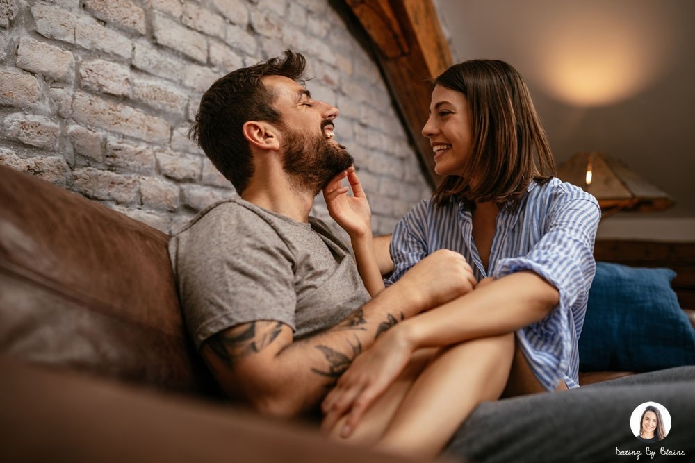 Woman happily sitting on a man's lap on a coach, touching his face, cuddling