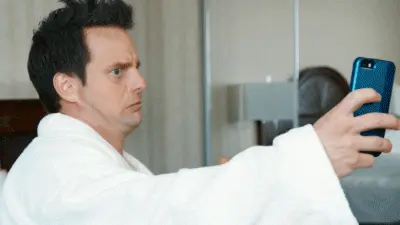Man in a bathrobe holding a smartphone, posing for a silly selfie photo