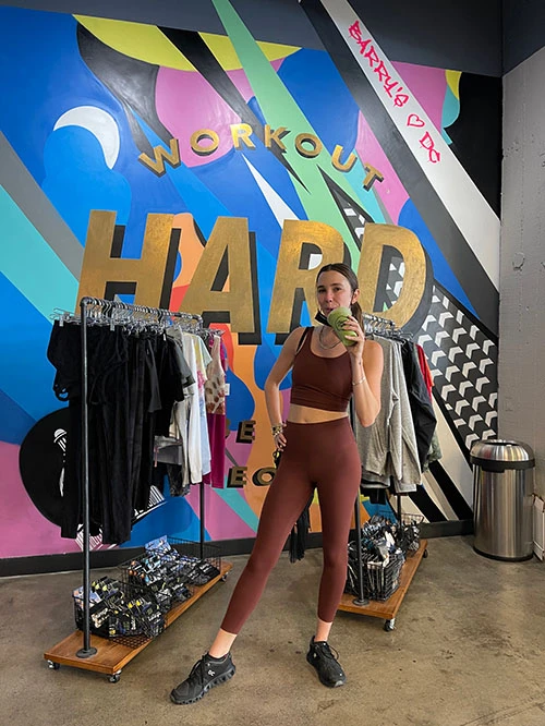 Blaine in red workout outfit drinking a smoothie at Barry's Bootcamp