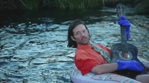 Gif of a man strumming a guitar while sitting in an inflatable raft on a river