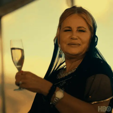 Gif of Jennifer Coolidge raising her glass of wine, toasting