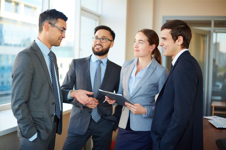 Four business professionals in suits discussing work together in a modern office.