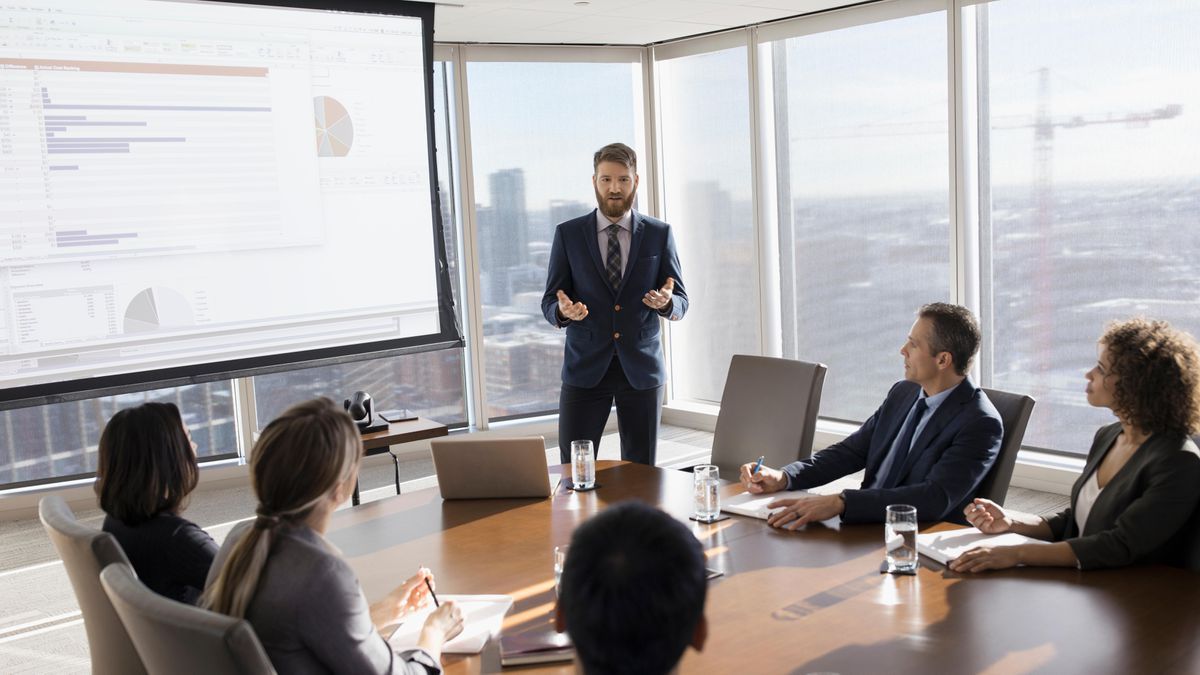 Businessman presenting data charts to colleagues in a modern high-rise conference room.
