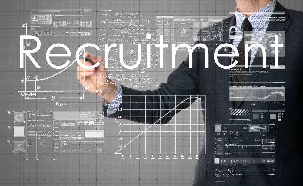 Businessman drawing the word "Recruitment" over futuristic recruiting-technology graphics.