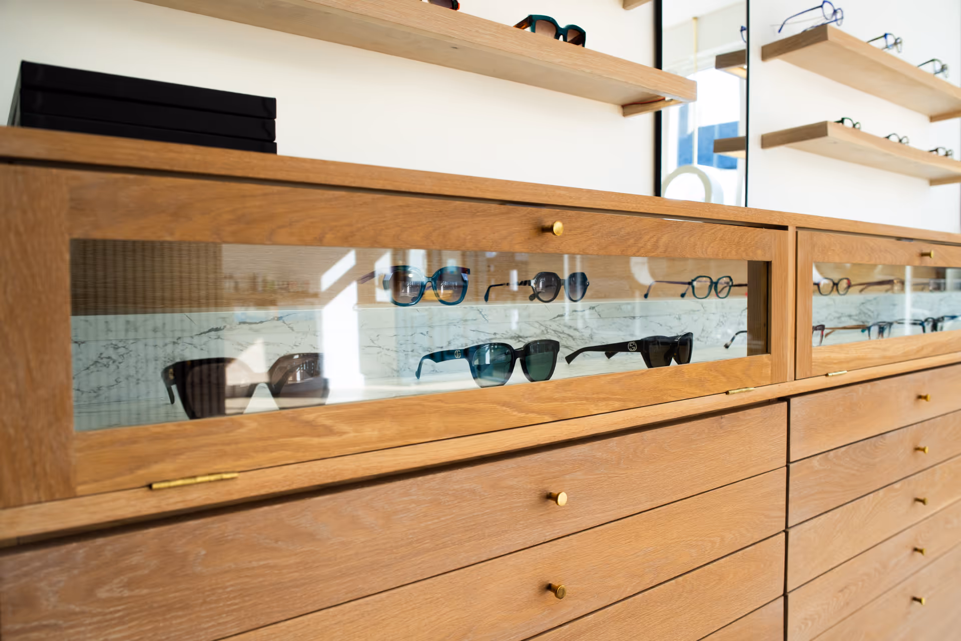 Wooden display cabinet with glass cases showcasing various designer sunglasses