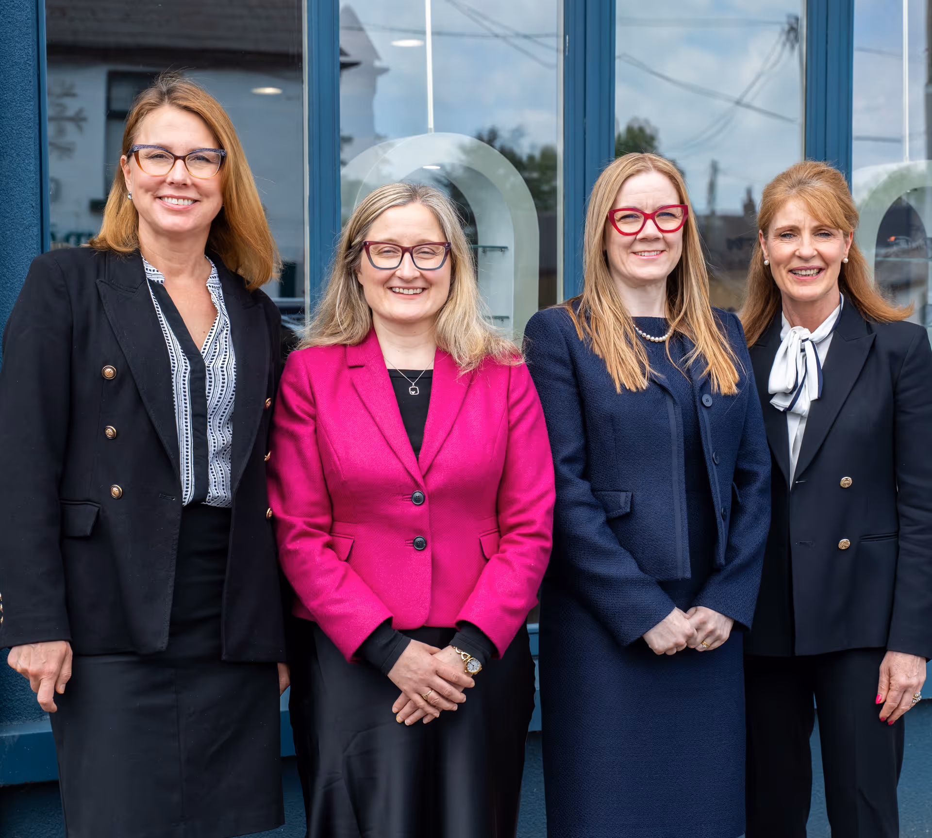 Four professional women in business attire smiling together outside