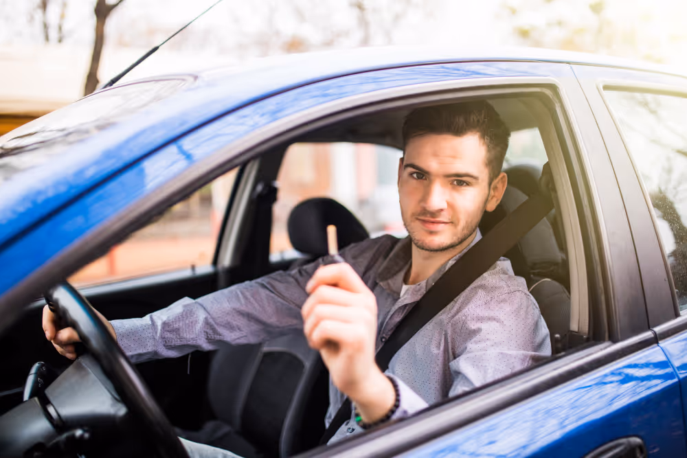 Smiling driver in blue car giving thumbs up while wearing seatbelt