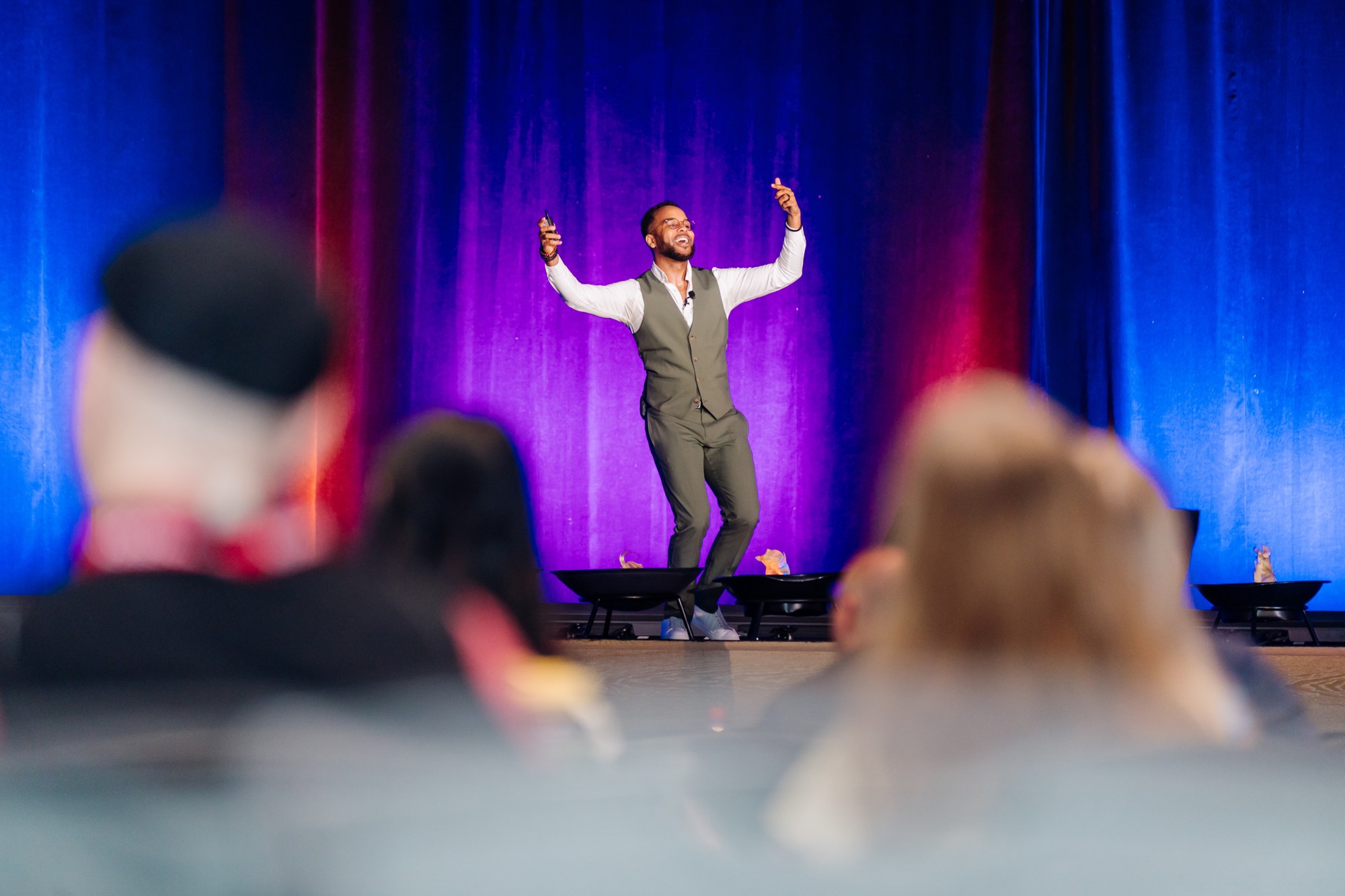 Darryl on stage with his arms raised in front of a full room