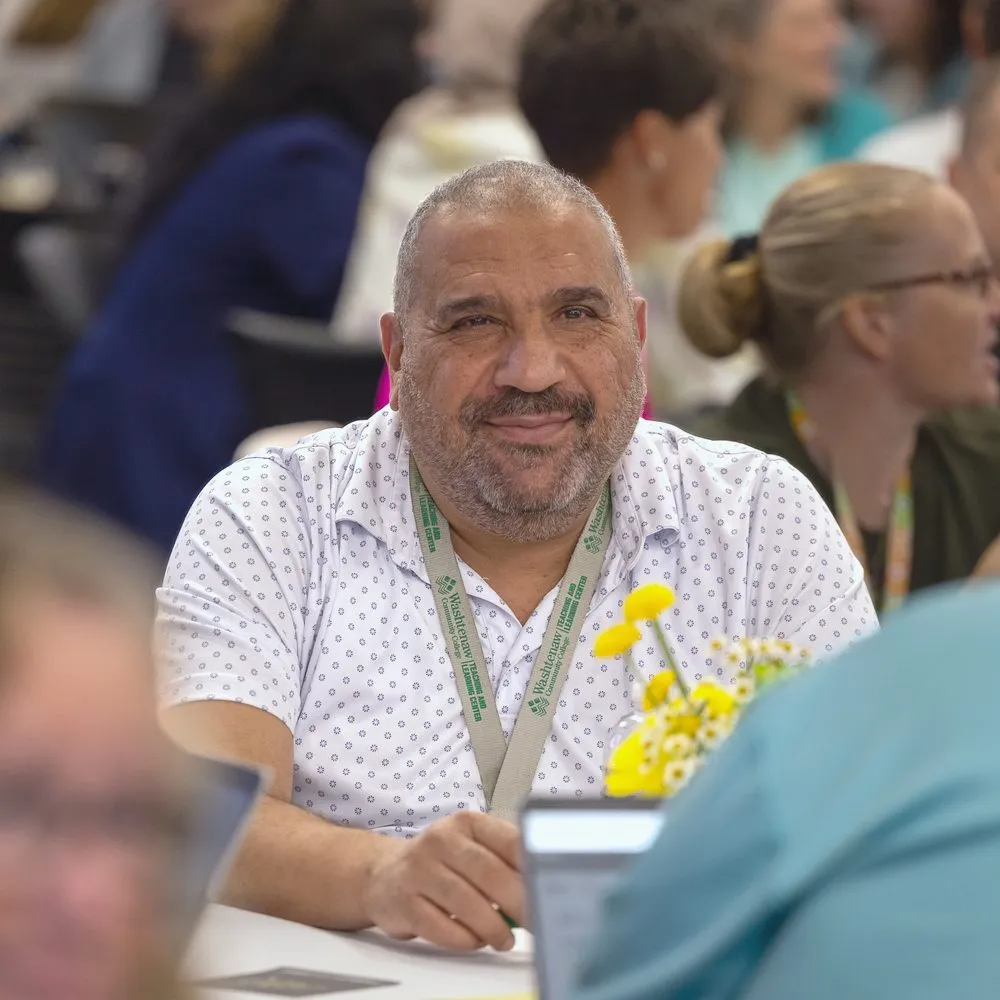 An educator smiling at his table during a keynote
