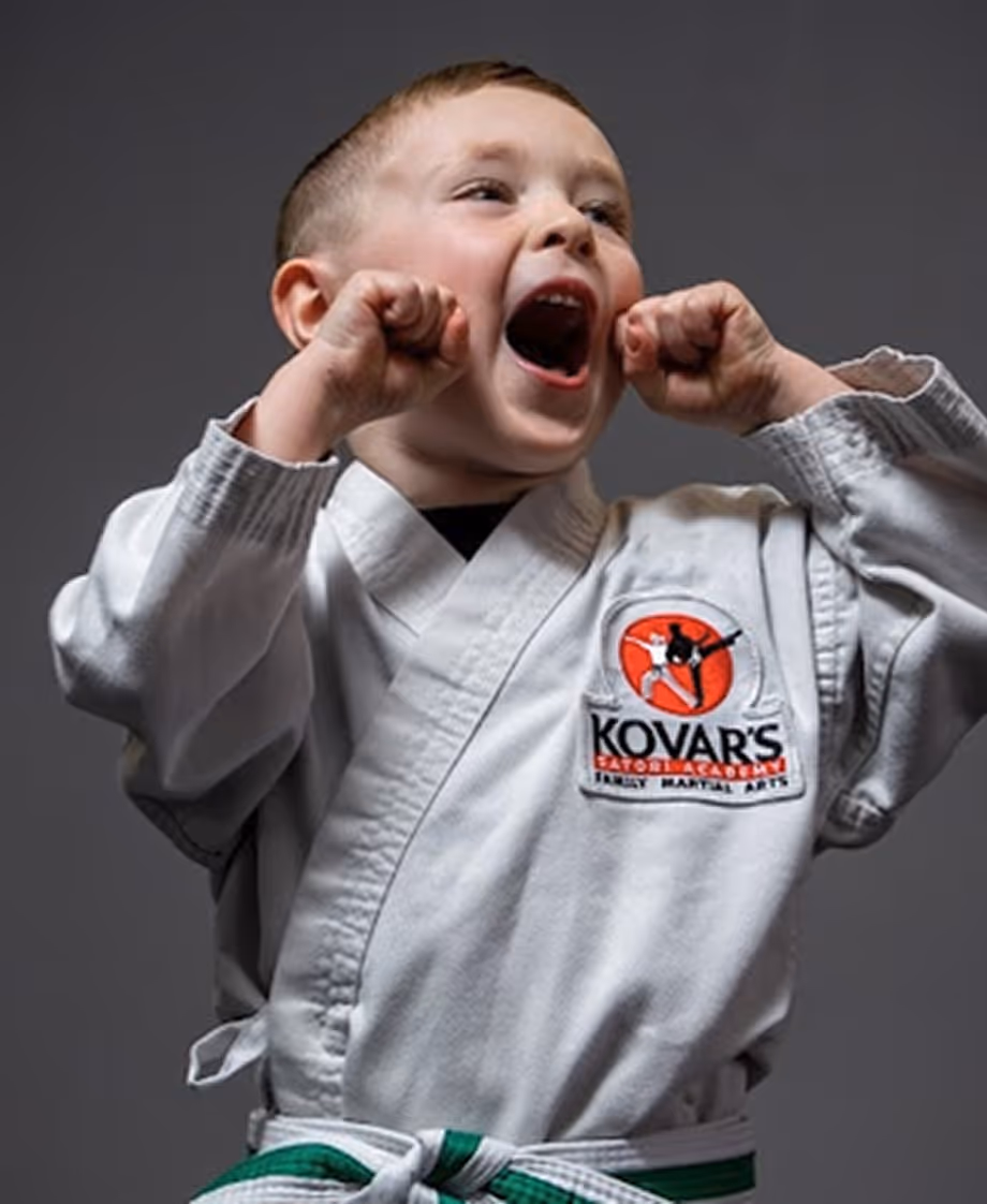Young boy in a martial arts uniform with a green belt cheering with fists raised by his face.