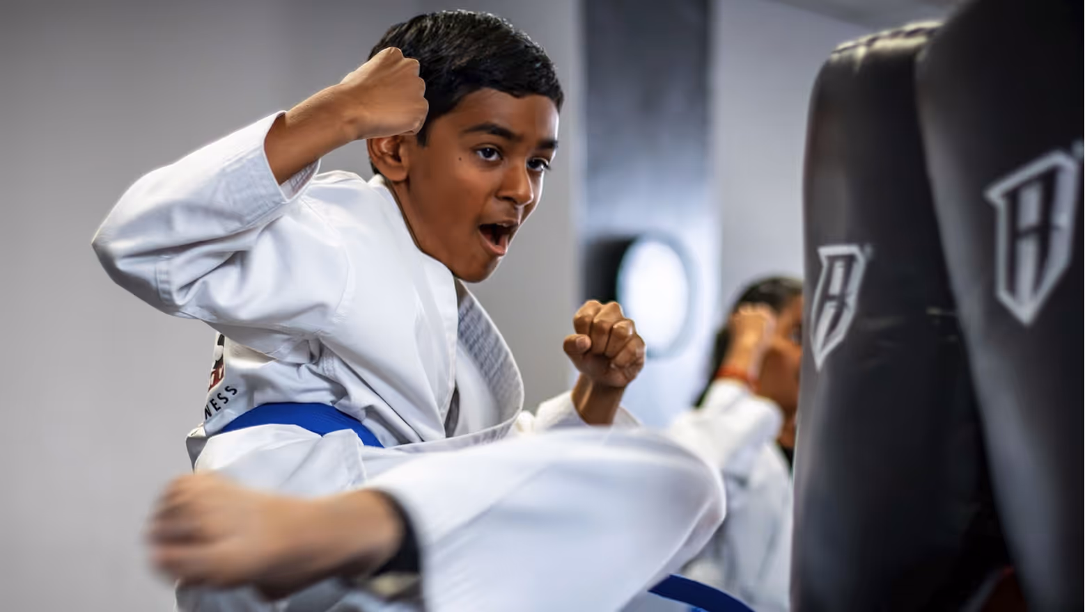 Boy in a white karate uniform with a blue belt performing a high kick during martial arts training.