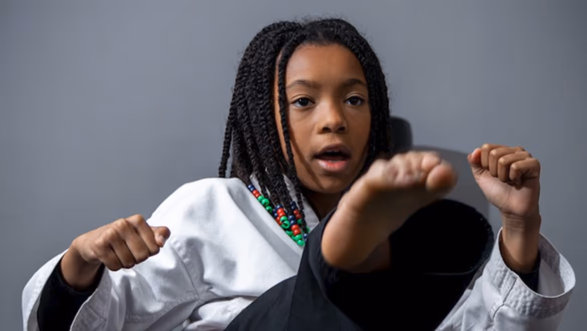 Young girl with braided hair practicing a martial arts kick wearing a white karate uniform.
