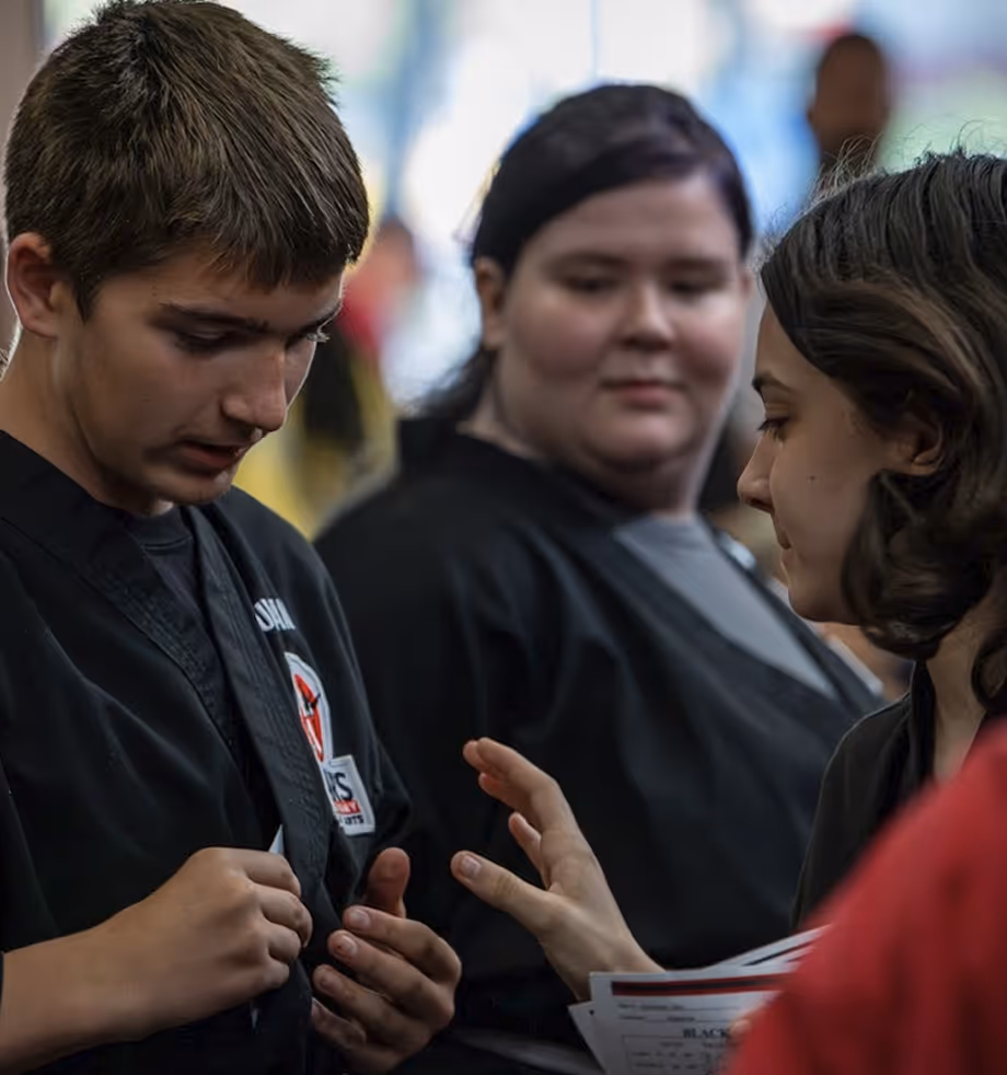 Three people wearing martial arts uniforms, one adjusting their belt while another holds a certificate.