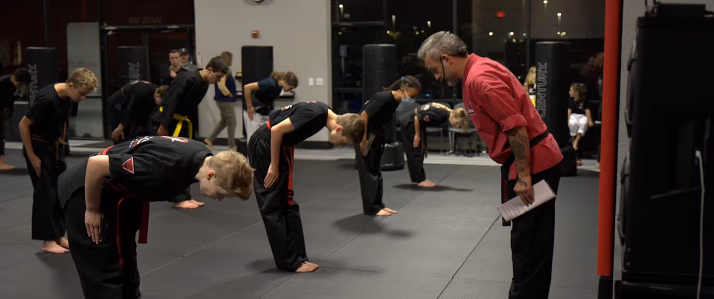 Martial arts instructor and students bowing on a training mat inside a dojo.
