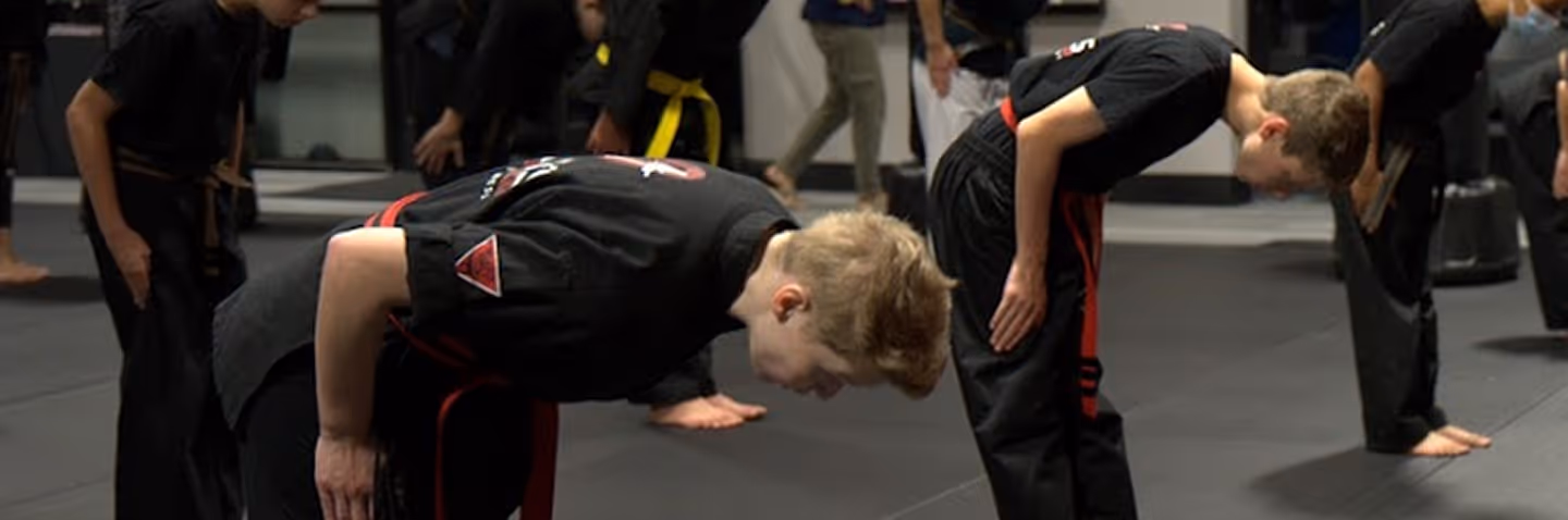 Martial arts students bowing in a dojo wearing black uniforms with colored belts.