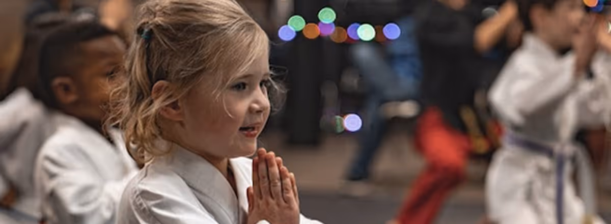 Young children in white karate uniforms practicing martial arts indoors.