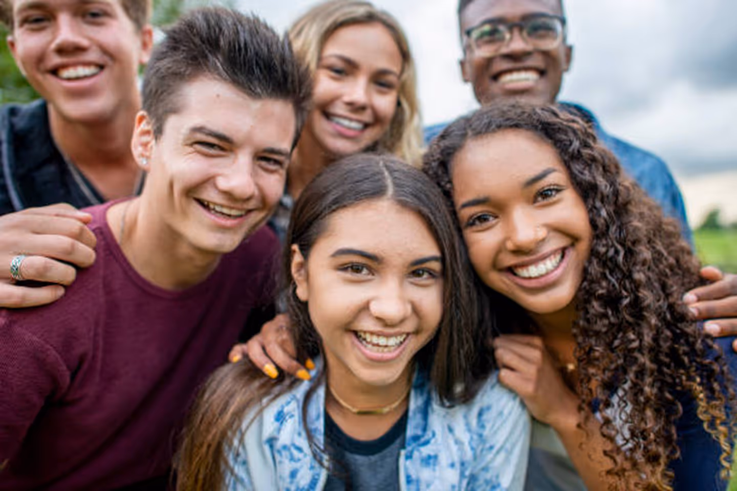 Group of six diverse young adults smiling and posing closely outdoors.