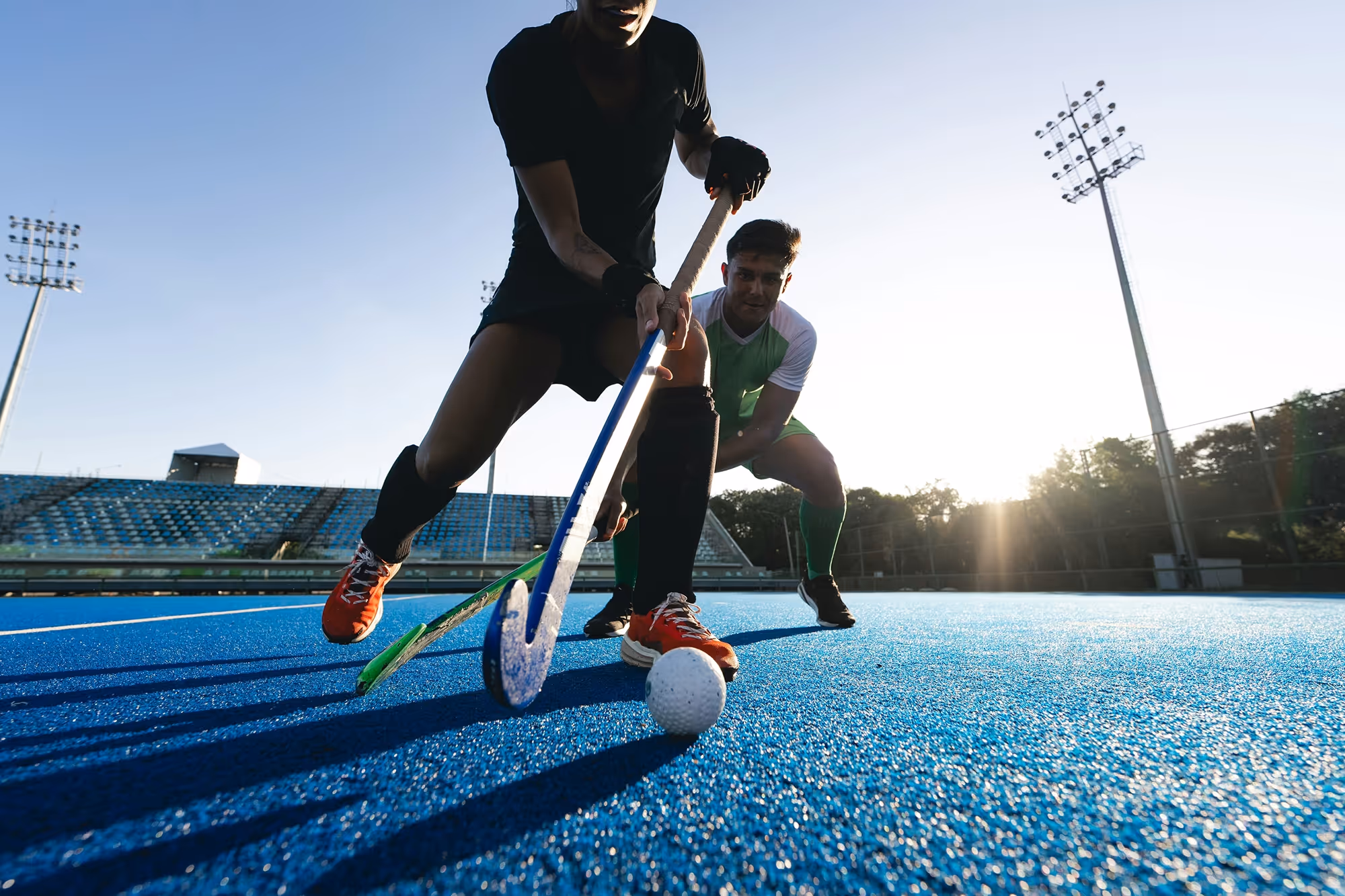 Zwei Hockeyspieler kämpfen um den Ball auf beleuchtetem Spielfeld